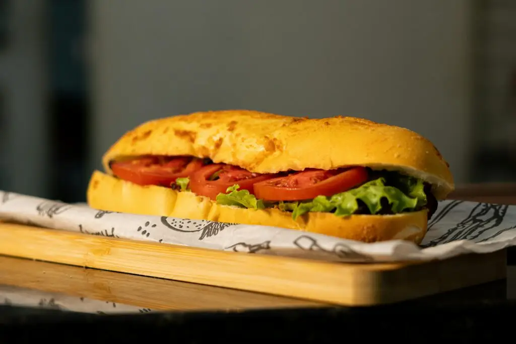 Close-up of a sandwich with tomato slices and lettuce on a toasted bun, resting on a wooden board.
